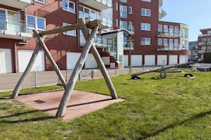 A playground with a swing set and a slide in front of a multi-story building with balconies. - Holiday apartment with 1 bedroom (Cuxhaven)