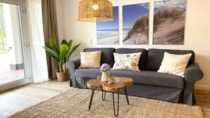 En stue med en grå sofa, et vævet sofabord og en hængende lampe.