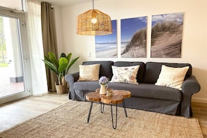 A living room with a grey sofa, a woven coffee table, and a hanging light fixture. - Holiday apartment with 1 bedroom (Cuxhaven)