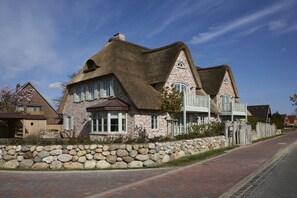 A stone house with a thatched roof, a stone wall, and a paved driveway. - Holiday apartment in Büsum with swimming pool (Büsum)