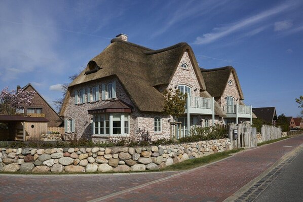 A stone house with a thatched roof, a stone wall, and a paved driveway. - Holiday apartment in Büsum with swimming pool (Büsum)
