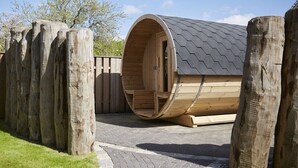 Una estructura cilíndrica de madera con techo inclinado, terraza de madera y sendero pavimentado que la conduce.