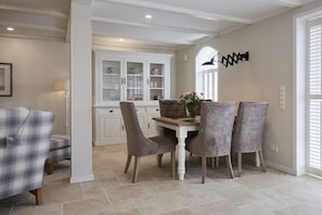 A dining area with a white table and four chairs, a cabinet with glass doors, and a wall-mounted light fixture. - Holiday apartment in Büsum with swimming pool (Büsum)