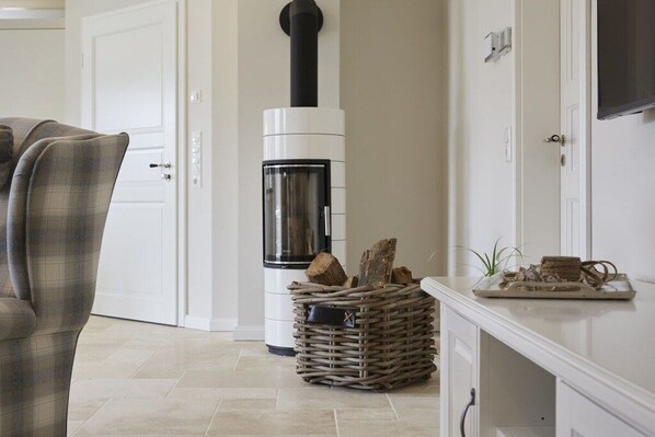Een kamer met een open haard, een bank, een rieten mand vol houtblokken en een dienblad met decoratieve spullen.