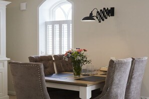 Een eetgedeelte met een tafel, stoelen, een vaas met bloemen en een wandlamp.