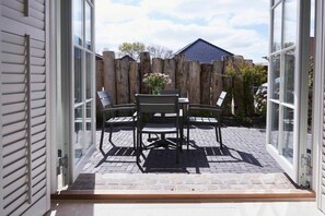 An open patio with a table and chairs, a wooden fence, and a house in the background. - Holiday apartment in Büsum with swimming pool (Büsum)
