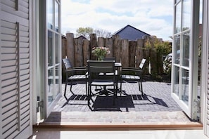 En öppen uteplats med ett bord och stolar, ett trästaket och ett hus i bakgrunden.