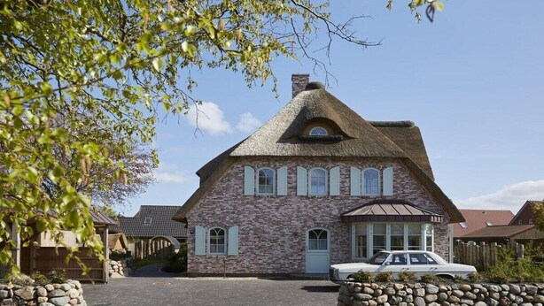 A stone house with a thatched roof, a car parked in front, and a stone wall. - Holiday apartment in Büsum with swimming pool (Büsum)