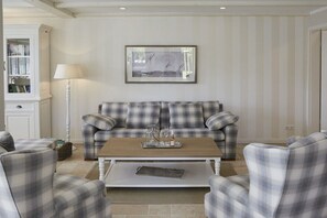 Ein Wohnzimmer mit einem Karo-Sofa, passenden Sesseln, einem Couchtisch und einem gerahmten Bild an der Wand.
