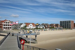 Eine Küstenstadt mit einem Steg, Strand und verschiedenen Gebäuden, darunter ein Hotel mit einer Flagge.