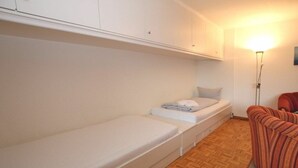 Une petite pièce comprenant un lit simple, une chaise et un luminaire fixé au mur.