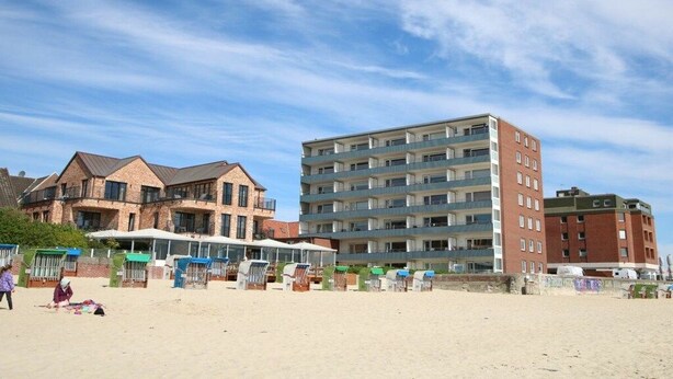 Un hôtel en bord de mer, avec plusieurs étages, des équipements de plage et un ciel dégagé.