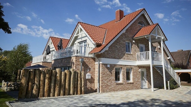 A two-story house with a brick exterior, a red-tiled roof, and a wooden fence. - Holiday apartment in Büsum with swimming pool (Büsum)