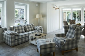 A living room with a sofa, armchair, and ottoman, a coffee table, and a lamp. - Holiday apartment in Büsum with swimming pool (Büsum)