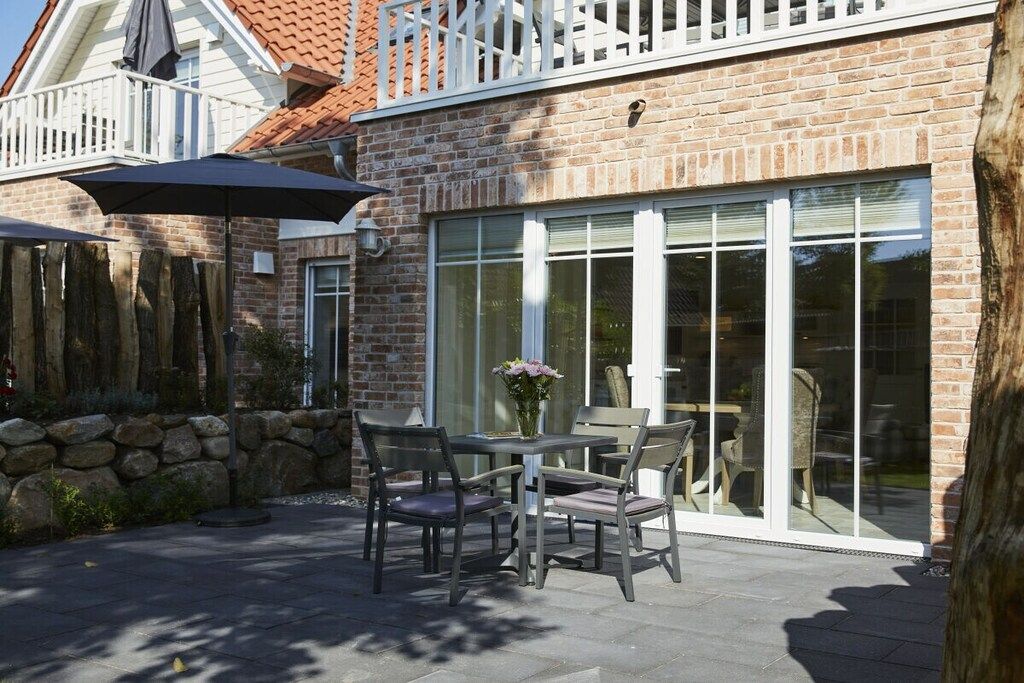 A patio with a table and chairs, a stone wall, and a glass door leading inside.