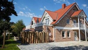 A two-story house with a red-tiled roof, white balconies, and a stone wall. - Holiday apartment in Büsum with swimming pool (Büsum)