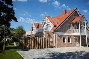A two-story house with a red-tiled roof, white balconies, and a stone wall. - Holiday apartment in Büsum with swimming pool (Büsum)