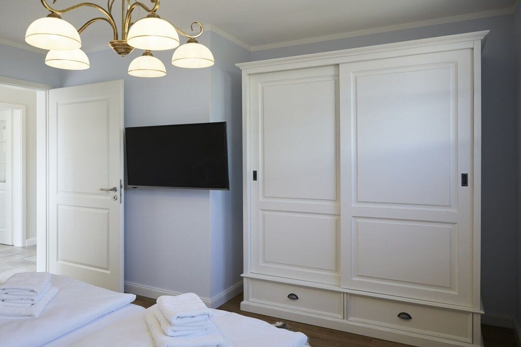 Une chambre dotée d’une grande armoire, d’un téléviseur à écran plat fixé au mur et d’un lit agrémenté de serviettes blanches soigneusement pliées.