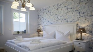 A bedroom with a white bed, two bedside tables, and a window with blinds. - Holiday apartment in Büsum with swimming pool (Büsum)