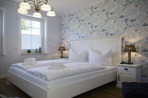 A bedroom with a white bed, two bedside tables, and a window with blinds. - Holiday apartment in Büsum with swimming pool (Büsum)