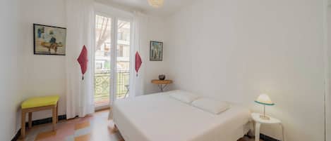Un dormitorio con cama, una mesita de noche con lámpara, una silla y dos cuadros en la pared.