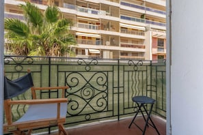 A balcony with a metal fence, a wooden chair, a small table, and a palm tree in the background. - a/c 2BDR/4P appartement - Cannes center (Cannes)