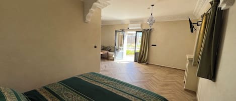 A spacious bedroom with a large bed, a ceiling fan, and a view through an open door to a balcony.
