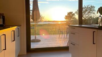 A modern kitchen with a large window, wooden flooring, and a view of the outdoors.