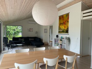 Ett modernt vardagsrum med ett matbord i trä, vita stolar, en svart soffa och en stor tavla på väggen.