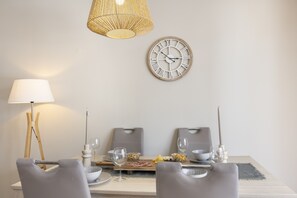 A dining area with a table set for two, a wall clock, and a hanging light fixture. - Casa do Mar Aromas Condomínio by CoolHouses (Burgau)