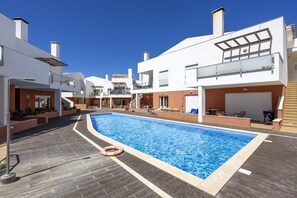 Un edifici residencial modern amb piscina, mobiliari exterior i un cel blau clar.