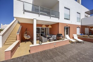 Un edificio moderno de dos pisos con un área exterior techada que cuenta con una mesa de comedor, sillas de lounge y una silla colgante.