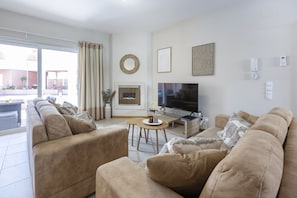A living room with beige sofas, a flat-screen TV, a fireplace, and a dining area with a table and chairs. - Casa do Mar Aromas Condomínio by CoolHouses (Burgau)