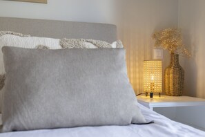 A bed with a grey pillow, a textured grey headboard, and a bedside table with a woven lamp and a vase with dried flowers. - Casa do Mar Aromas Condomínio by CoolHouses (Burgau)