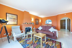 A living room with a sofa, armchair, coffee table, fireplace, and colorful rug. - CoolHouses Algarve Luz | Ramalhete T2 (Luz)