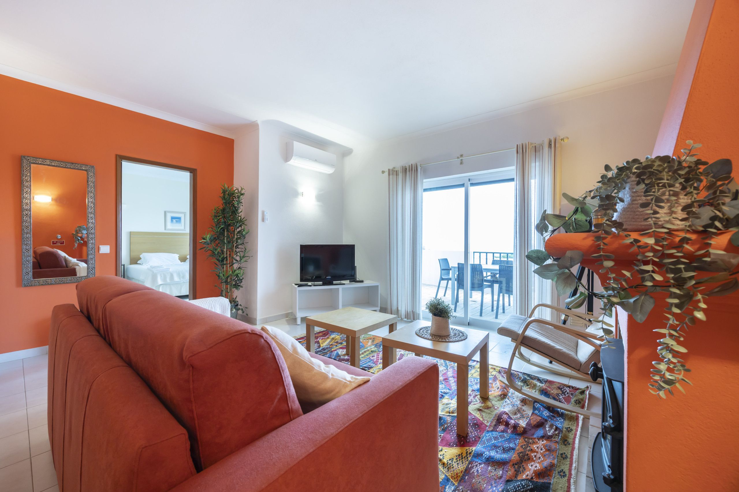 Un salon moderne comprenant un canapé, un téléviseur, un coin repas et un balcon aménagé avec du mobilier d’extérieur.