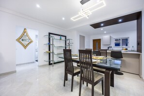 A modern dining area with a glass table, dark wooden chairs, and a kitchen in the background. - The Penthouse Waterside by CoolHouses (Luz)