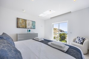 Ein modernes Schlafzimmer mit einem großen Bett, Meerblick und einem Bild an der Wand.