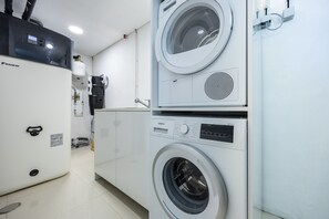 A laundry room with stacked washing machines, a water heater, and a control panel. - Vila Camilo Ponta do Farol by CoolHouses (Lagos)