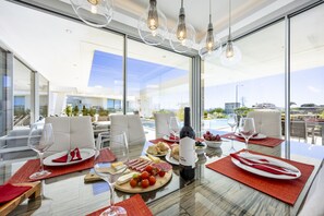 A modern dining area with a glass table, white chairs, and a view of the outdoors. - Vila Camilo Ponta do Farol by CoolHouses (Lagos)