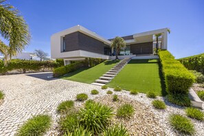 A modern two-story house with a paved driveway, a well-maintained lawn, and a variety of plants. - Vila Camilo Ponta do Farol by CoolHouses (Lagos)