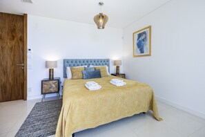 A neatly arranged bedroom with a bed, two bedside tables, a nightstand, a wall-mounted light fixture, and a framed artwork. - Vila Camilo Ponta do Farol by CoolHouses (Lagos)