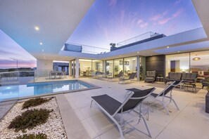 Ein moderner Außenbereich mit Pool, Liegestühlen und einem verglasten Essbereich.
