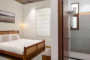 A bedroom with a wooden bed, a wall-mounted light, a window with blinds, and a door leading to a bathroom. - Wandr Indiranagar (BENGALURU)