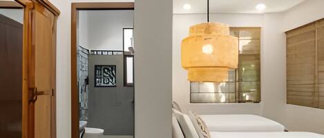 A modern bedroom with a bed, bedside tables, a hanging light fixture, and a window with blinds.