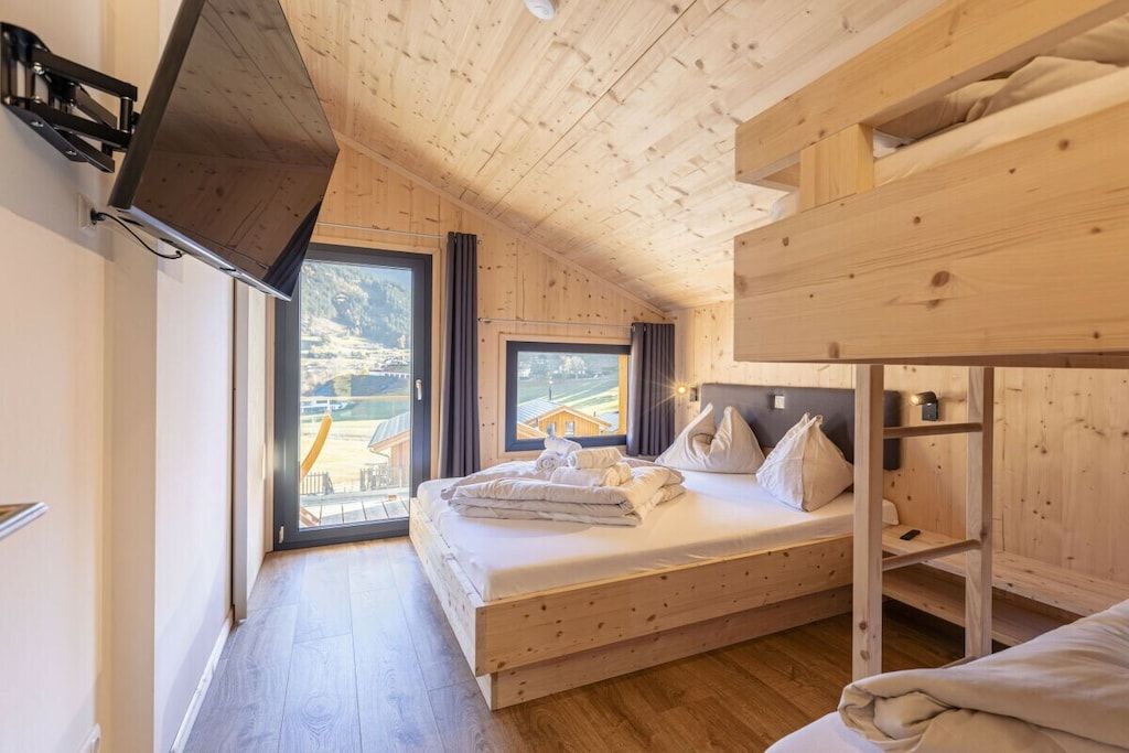Habitación tipo cabaña de madera con una cama, literas y un ventanal que ofrece vistas al exterior.