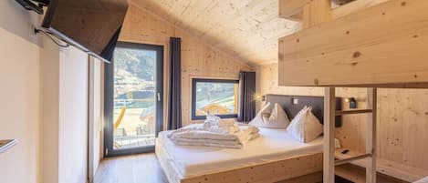 Habitación tipo cabaña de madera con una cama, literas y un ventanal que ofrece vistas al exterior.