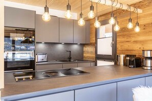 A modern kitchen with a central island, stainless steel appliances, and a wooden wall. - Cabin in Steinach am Brenner with sauna (Steinach am Brenner)