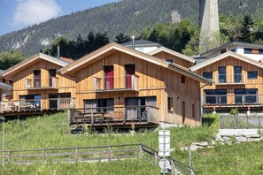 A row of wooden cabins with balconies, set against a mountainous backdrop.