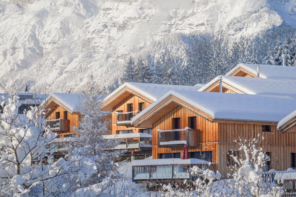 A wooden chalet-style building with balconies, surrounded by snow-covered trees and mountains.